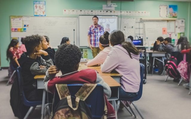 A teacher standing in front of a class of children who are sitting at desks